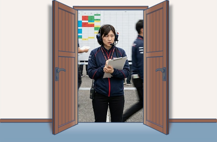 ヘッドセットを装着した女性チームマネージャーが、大型スケジュールボードの前で資料を確認しながらスタッフの動きを管理している様子。